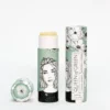 Lippenpflege in Stickform „caring Caroline“ von Queen of Green in mintfarbener, floral gestalteter Verpackung aus recyceltem Karton teilweise geöffnet mit sichtbar gelbem Balm; natürliche, vegane Lippenpflege im Stick.