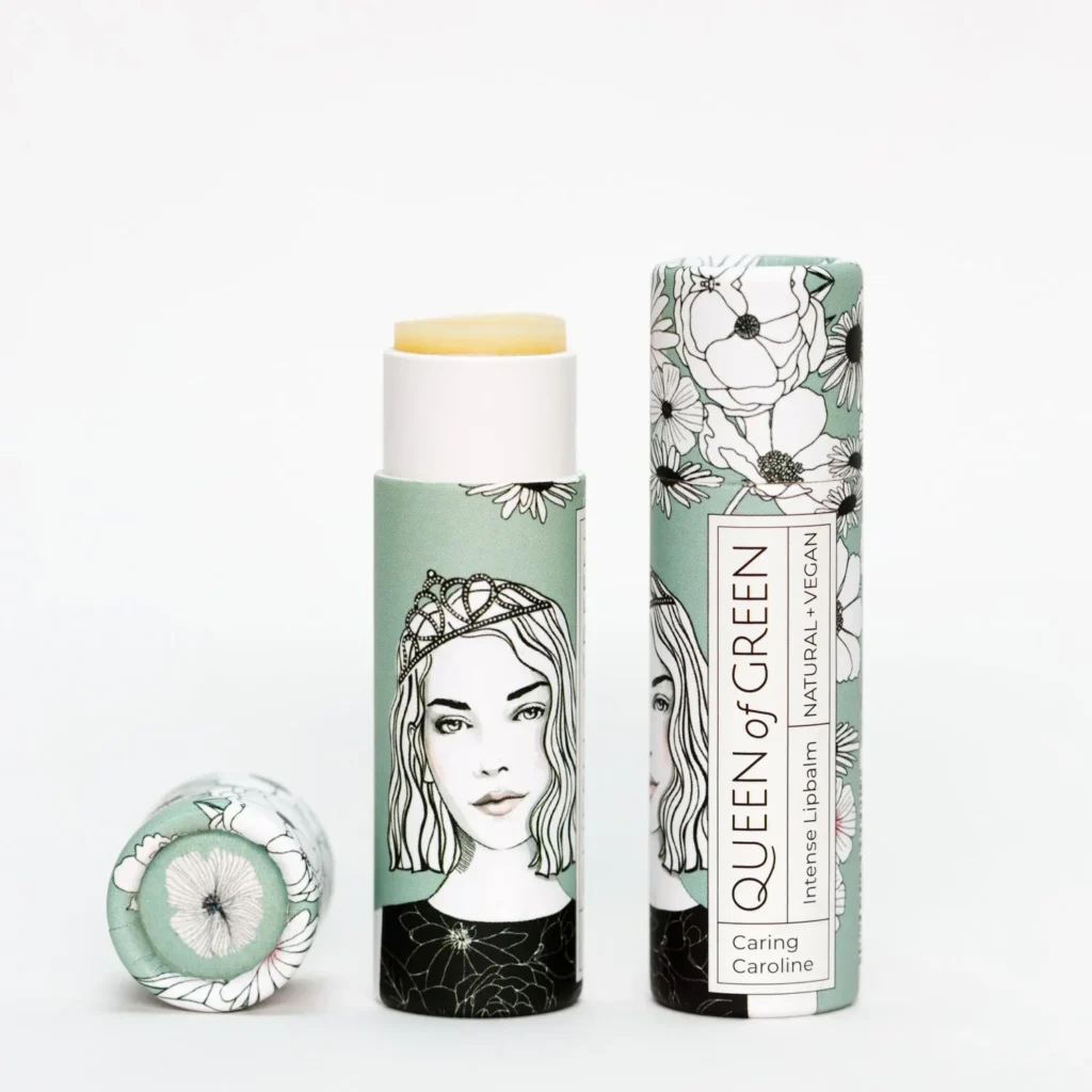 Lippenpflege in Stickform „caring Caroline“ von Queen of Green in mintfarbener, floral gestalteter Verpackung aus recyceltem Karton teilweise geöffnet mit sichtbar gelbem Balm; natürliche, vegane Lippenpflege im Stick.