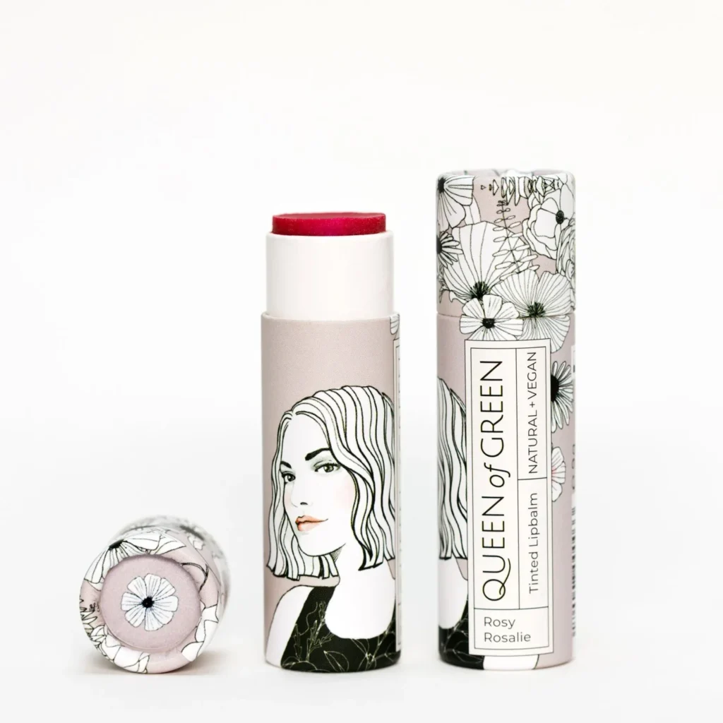 Getönter Lipbalm „Rosy Rosalie“ von Queen of Green in roséfarbener, floral gestalteter Verpackung aus recyceltem Karton teilweise geöffnet mit sichtbar rosarotem Balm; natürliche, vegane Lippenpflege im Stick.