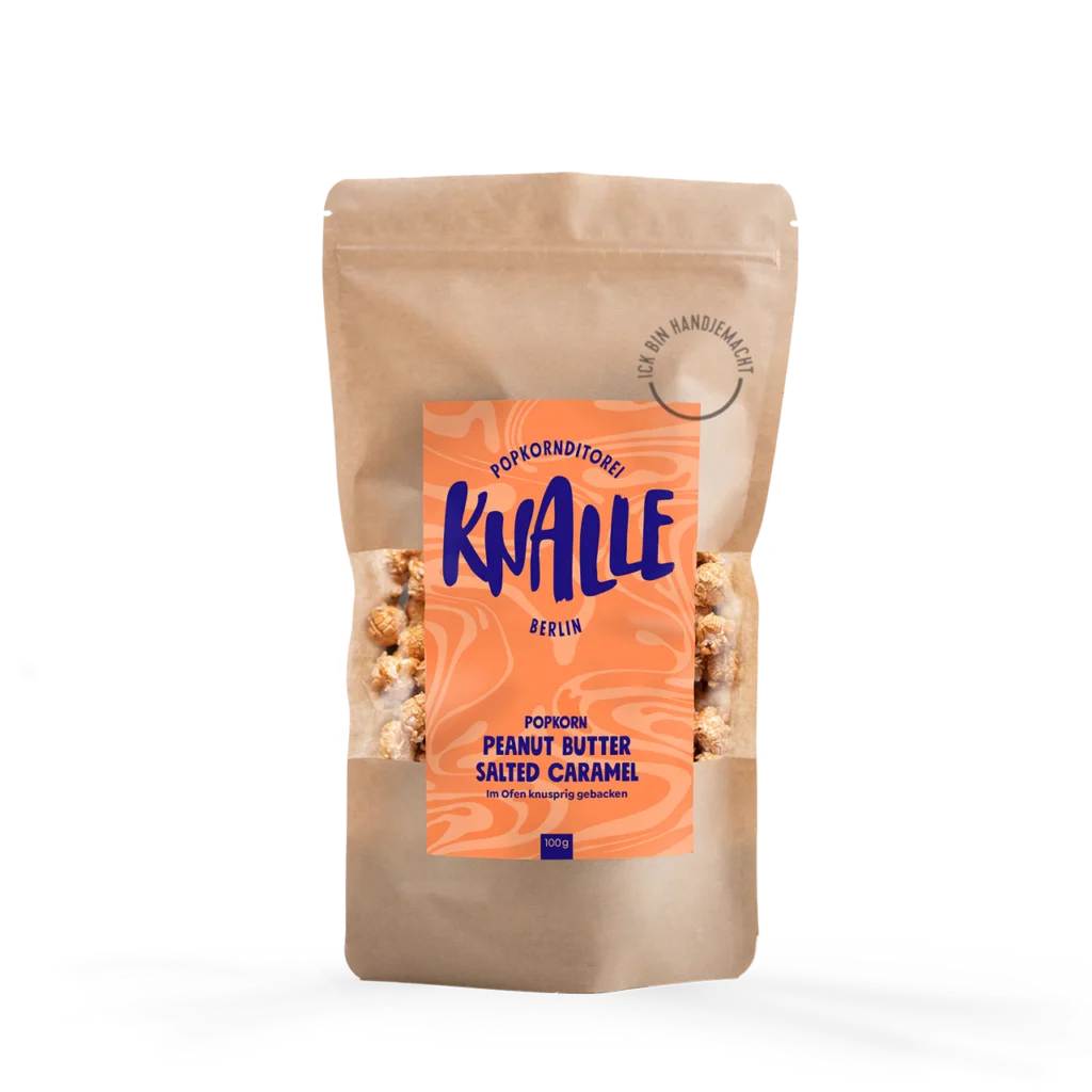 Das Bild zeigt eine Popkorn Verpackung - wiederverschließbare braune Tüte. Das Etikett ist Flamingoorange mit blauer Schrift