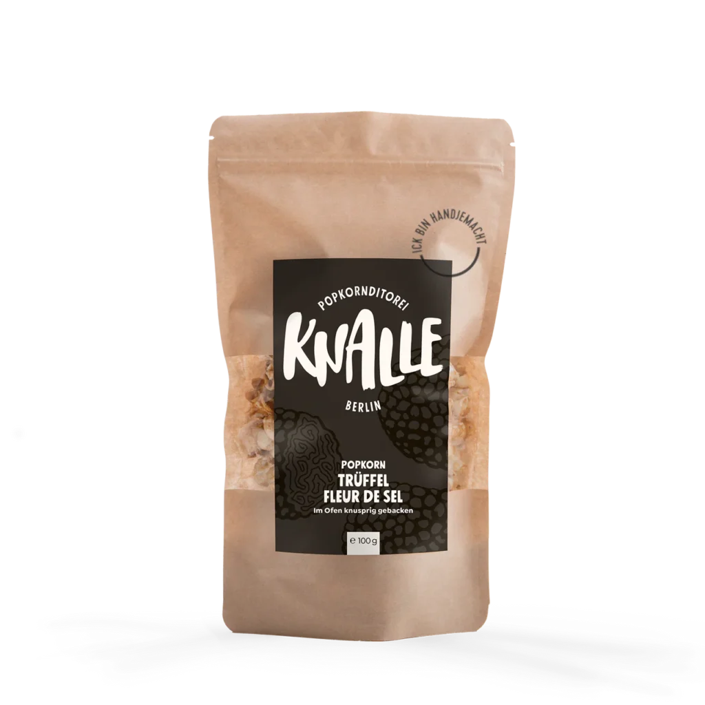 Das Bild zeigt eine Popkorn Verpackung - wiederverschließbare braune Tüte. Das Etikett ist schwarz mit weißer Schrift