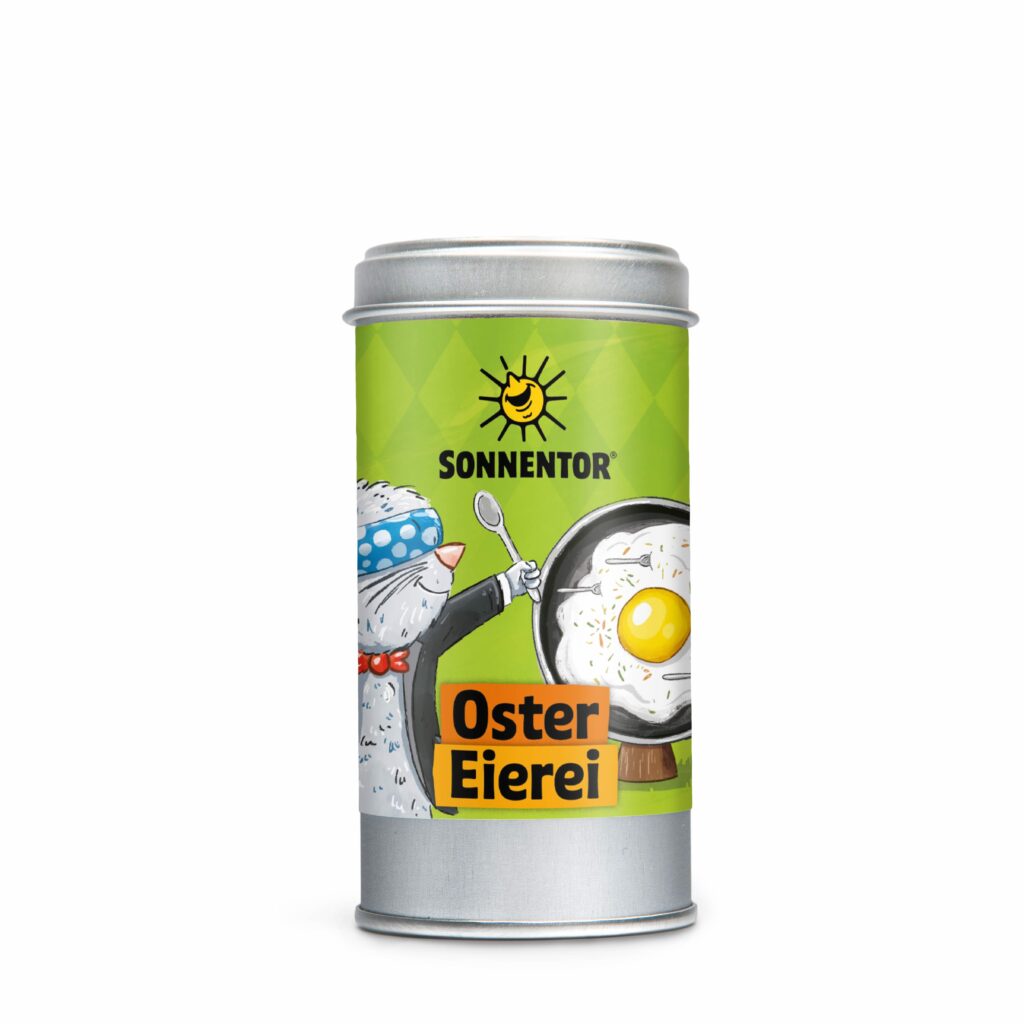 Gewürzmischung: Das Bild zeigt eine Metalldose mit grünem Etikett der Marke Sonnentor mit der Aufschrift ‚Oster Eierei‘, illustriert mit einer fröhlichen Tierfigur, die einen Löffel hält, und einer Pfanne mit Spiegelei.