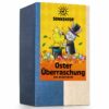 Das Foto zeigt eine rechteckige Tee Packung aus Karton. Auf der Verpackung zu sehen ist ein gezeichneter Osterhase, in Frack und Zylinder, der ein Küken aus dem Zylinder zaubert. Auf dem orangenem Grasboden verteilen sich bunte Ostereier