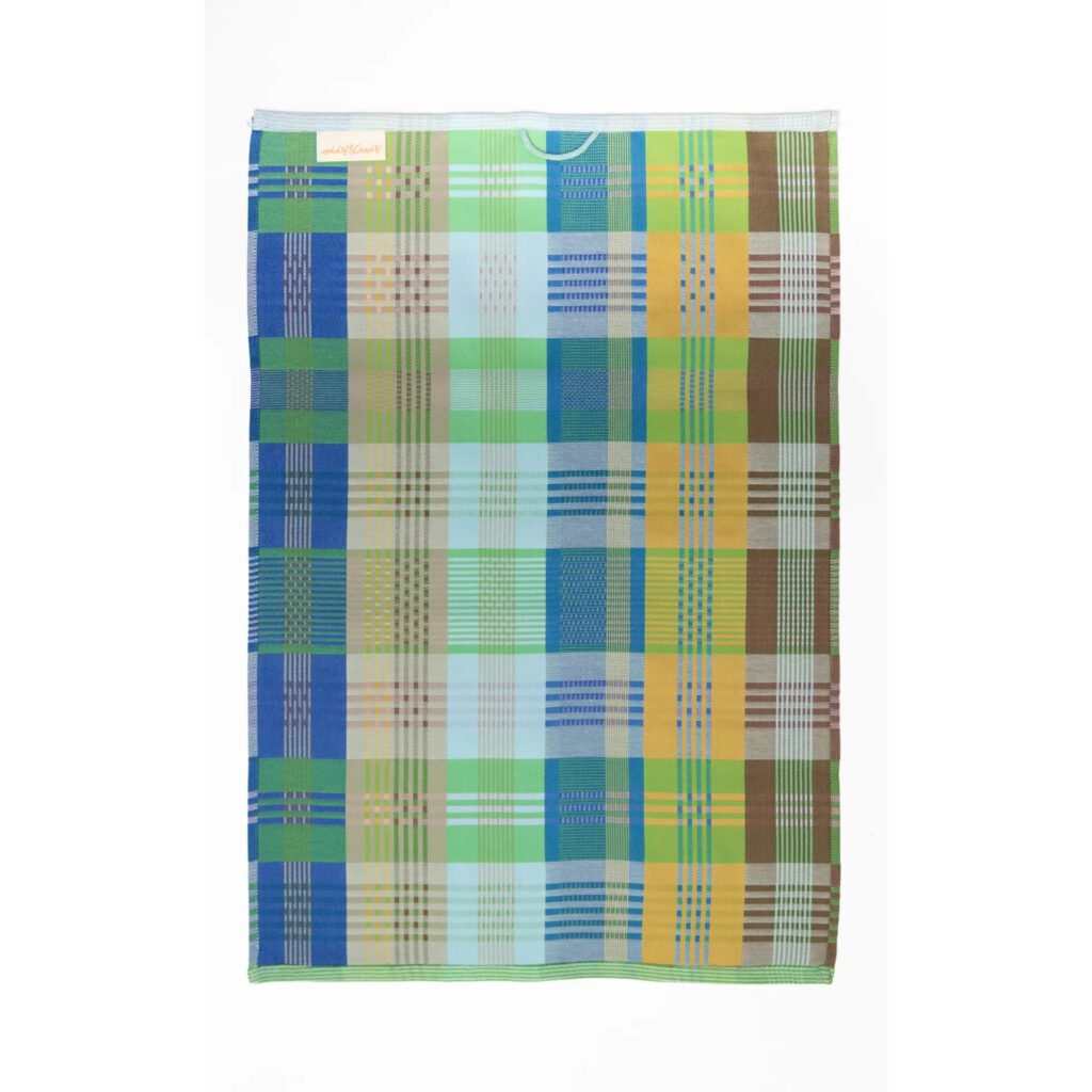 Bunt kariertes Geschirrtuch mit großflächigem Patchwork-Muster in Blau-, Grün-,Gelb-, Hellblau- und Brauntönen, mit weißer Aufhängeschlaufe oben mittig und schmalen, gestreiften Abschlusskanten.