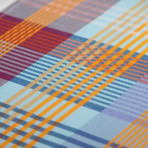 Geschirrtuch - wild weave #95A 9 Bunt kariertes Geschirrtuch mit großflächigem Patchwork-Muster in Blau-, Rot-, Gelb-, Orange- und Lilatönen, mit orangefarbener Aufhängeschlaufe oben mittig und schmalen, gestreiften Abschlusskanten.